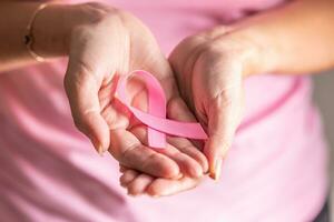 Detail of woman holding pink ribbon in her folded palms, the symbol of breast cancer prevention need photo