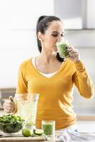 A young woman enjoys a spinach smoothie she made herself. She drinks a vegetable energy drink photo