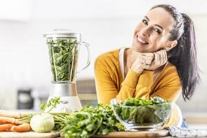 un joven mujer prepara un energía bebida desde Fresco vegetales utilizando un licuadora. foto