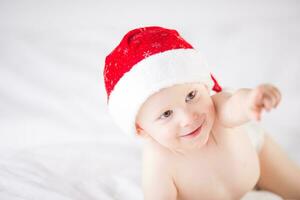 Cute baby boy with santa hat on bed under white duvet photo