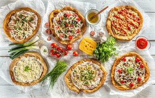 A close up a set of hungarian traditional langos with crusty garlic edges served with vegetables, cream sausages, herbs, grated, cheese, ketchup and dips and oil photo