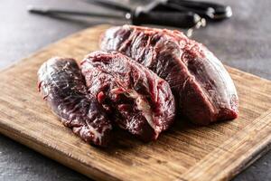 Large uncut pieces of raw beef shank on a chopping board with knives in the background photo