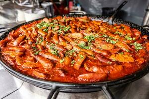 Large street food pan full of red sausage stew with parsley on top by the vendor photo