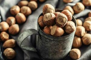 Close up of a vintage metallic mug full of hazelnuts with more nuts on a textile table cloth around it photo