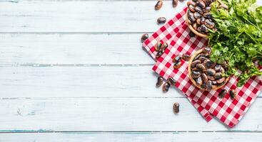 Uncooked beans in wooden bowles  with parsley herbs on kitchen table photo