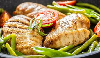 Close up of juicy chicken breasts, spring peas, green beans and cherry tomatoes in a skillet with black pepper and fresh rosemary seasoning photo