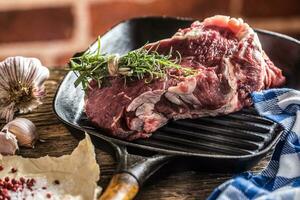 Raw beef steak in grill pan with salt pepper garlic and herbs on wooden table photo