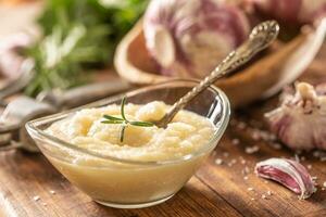 Garlic paste in a glass bowl with peeled garlic, salt, crusher and garlic heads photo