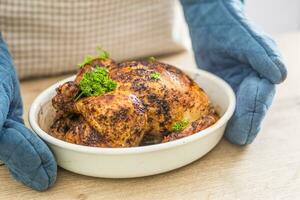 Whole roasted chicken in a baking bowl holding in hands cook with gloves photo