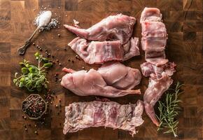 Top of view portioned rabbit legs and saddle with herbs and spices on butcher board photo