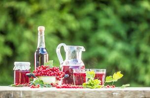 A selection of redcurrant products - marmalade jam syrup must and red vine on table in garden photo