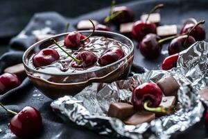 Fresh cherries in bowl with chocolate on dark tablecloth photo