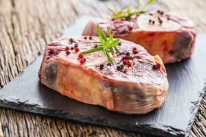 Two pieces raw beef shank on slate board and wooden table. photo