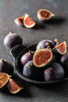 A few figs in a black bowl on an dark concrete table photo