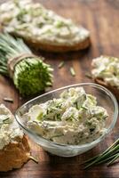 Portrait of a bowl of homemade cream cheese spread with chopped chives surrounded by bread slices with spread and a bunch of freshly cut chives photo