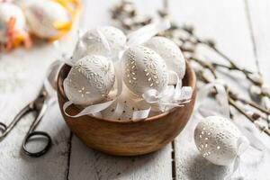 Handmade white easter eggs with willow catkins in a wooden bowl on wooden table photo