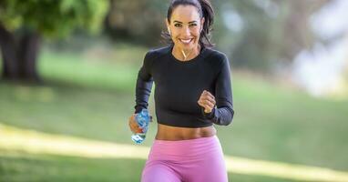 atractivo joven mujer corriendo en el parque con botella de agua foto