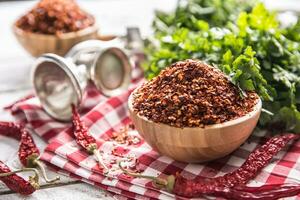 Dried and crushed chili peppers in wooden bowles with parsley herbs photo