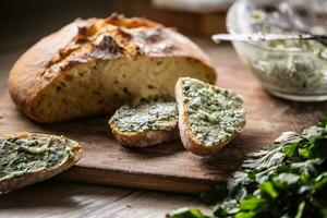 Crusty bread slices with herb butter spread on top with bowl of more mixed herb butter aside photo