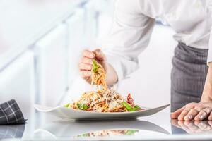 Chef in restaurant kitchen prepares and decorates meal with hands.Cook preparing spaghetti bolognese photo