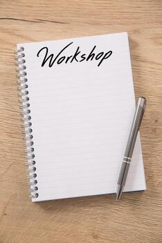 Blank spiral notebook with a Workshop headline and empty lines placed on a wooden table and a metallic silver pen positioned on top of it photo