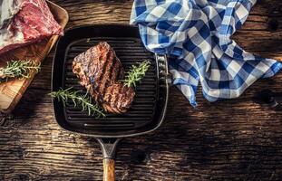 Grilled beef steak in grill pan with herbs rosemary on wooden table photo