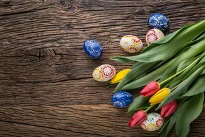 Easter. Hand made easter eggs and spring tulips on old wooden table. photo