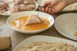 Detail of hand putting chicken meat in flour into eggs during making schnitzels photo