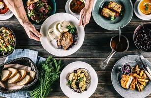 Chef Hand picking up a plate with meal from a top view of a table full of assortment meals , including soup,bread,salad, dumplings, schnizel, pasta lasagne and herbs photo