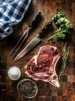 Rib eye steak with bone on butcher board with herbs salt pepper fork and knife photo