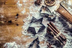 Top of view bakery table full of christmas aromatic ingredients star anise cinnamon dried orange flour cookery book and cookie cutters photo