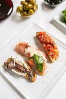 Tasty italian appetizer bruschettes with tomatoes anchovies prosciutto and mozarella photo