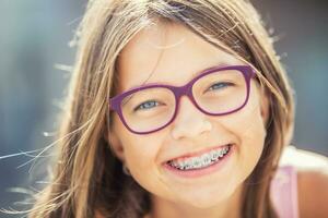 contento sonriente niña con dental tirantes y lentes. joven linda caucásico rubio niña vistiendo dientes tirantes y lentes foto