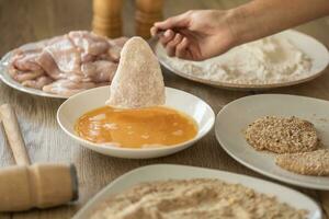 Breading of chicken breasts while putting them to flour and eggs during schnitzels making photo
