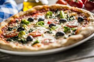 Irtalian pizza with broccoli spinach tomatoes olives and mozzarela or parmesan cheese. Mediterranean vegetarian meal photo