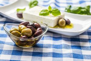 Green and red olives in bowl with olive oil and greek feta cheese in the background photo