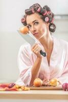 Good-looking girl looks at the camera with an onion stuck on the knife in her hand while standing in night dress in the kitchen photo