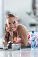 Detail of a smiling good-looking woman lying on the ground next to water bottle and dumbbells photo