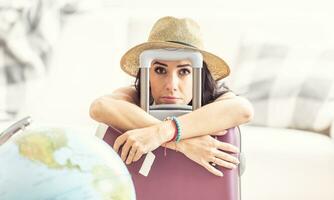 Unhappy female traveler holds suitcase placed next to a globe looking desperate due to travel restrictions photo