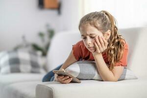 Bored young girl finds no more joy in scrolling on her phone as she sits at home on a couch photo