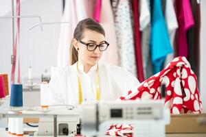 Tailor sweing dress in the workshop wearing classes and measuring tape around her neck photo