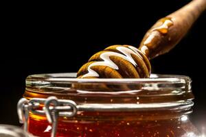 Jar of honey with dipper closeup - studio shot photo