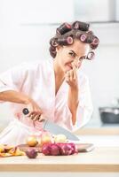 Woman in nightdress and hair rollers holds her nose from a smelly onion that she cuts on a cutting board photo