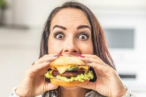 Woman with eyes wide open tries to bite into a big juicy hamburger photo