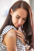 Vaccinated female looks at the plaster on her right shoulder photo