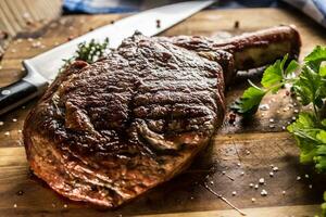Freshly grilled tomahawk steak on slate plate with salt pepper rosemary and parsley herbs photo