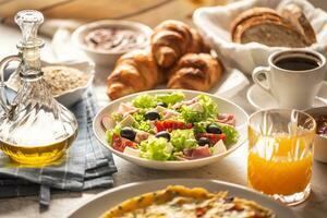 Broad assortment of food including omelette, croissants, salad, bread, oatmeal, jam, waffles, honey, choclate spread, coffee and orange juice served on a table photo