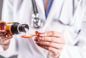 Hands of young woman doctor pouring medicinal syrup on spoon photo