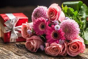 Beautiful bouquet of flowers with red gift on wooden table. photo