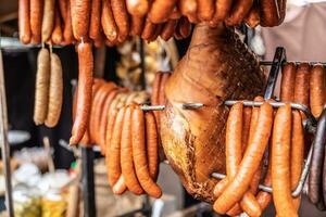 Cured meat products such as ham, sausages and frankfurters hanging at the market vendor booth outdoors photo
